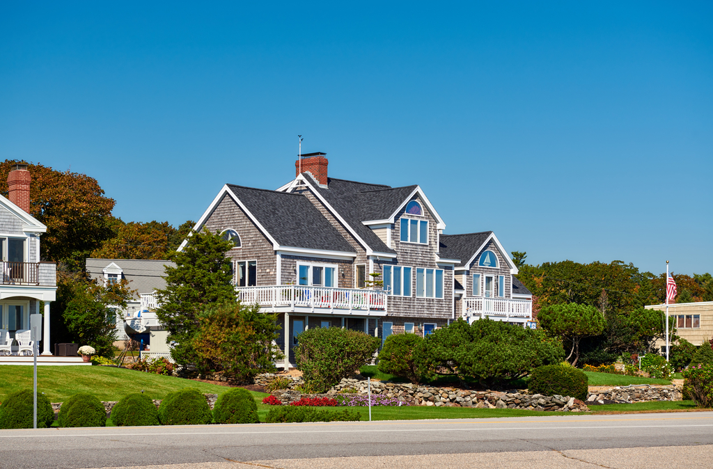 Luxury coastal home with grey shingle siding and white balconies overlooking a landscaped yard