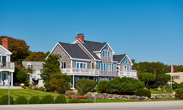 Luxury coastal home with grey shingle siding and white balconies overlooking a landscaped yard