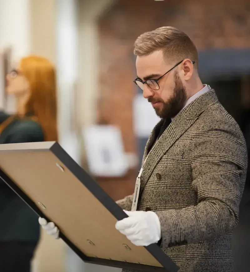 Professional art handler wearing white gloves carefully inspecting a framed piece of artwork for secure transport or installation