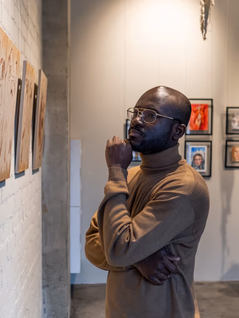 Art collector or gallery curator in a brown turtleneck thoughtfully observing paintings in an art gallery setting