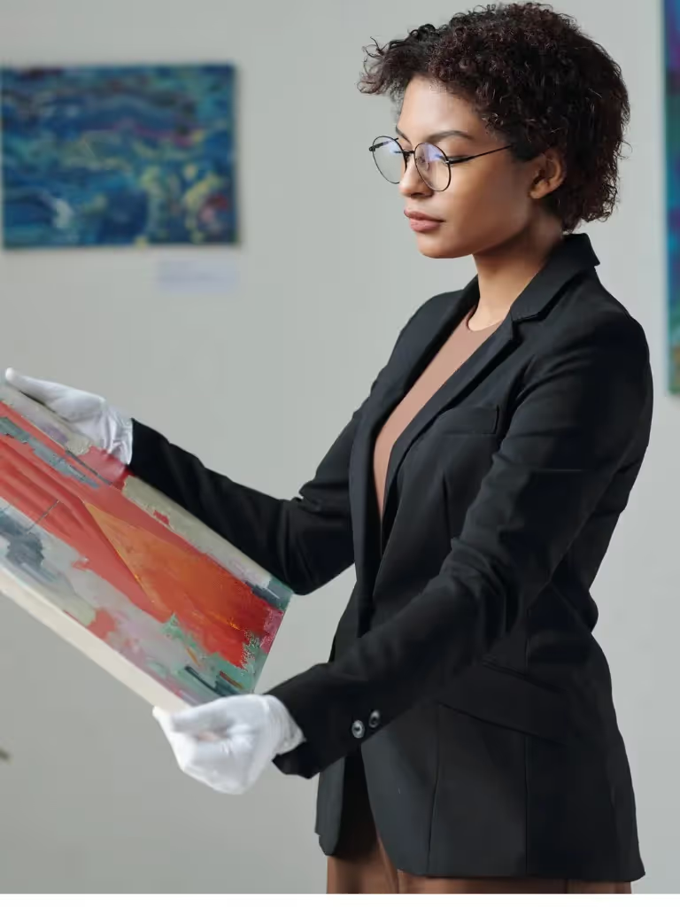 Professional female art gallery owner wearing white gloves while carefully handling an abstract canvas painting for exhibition