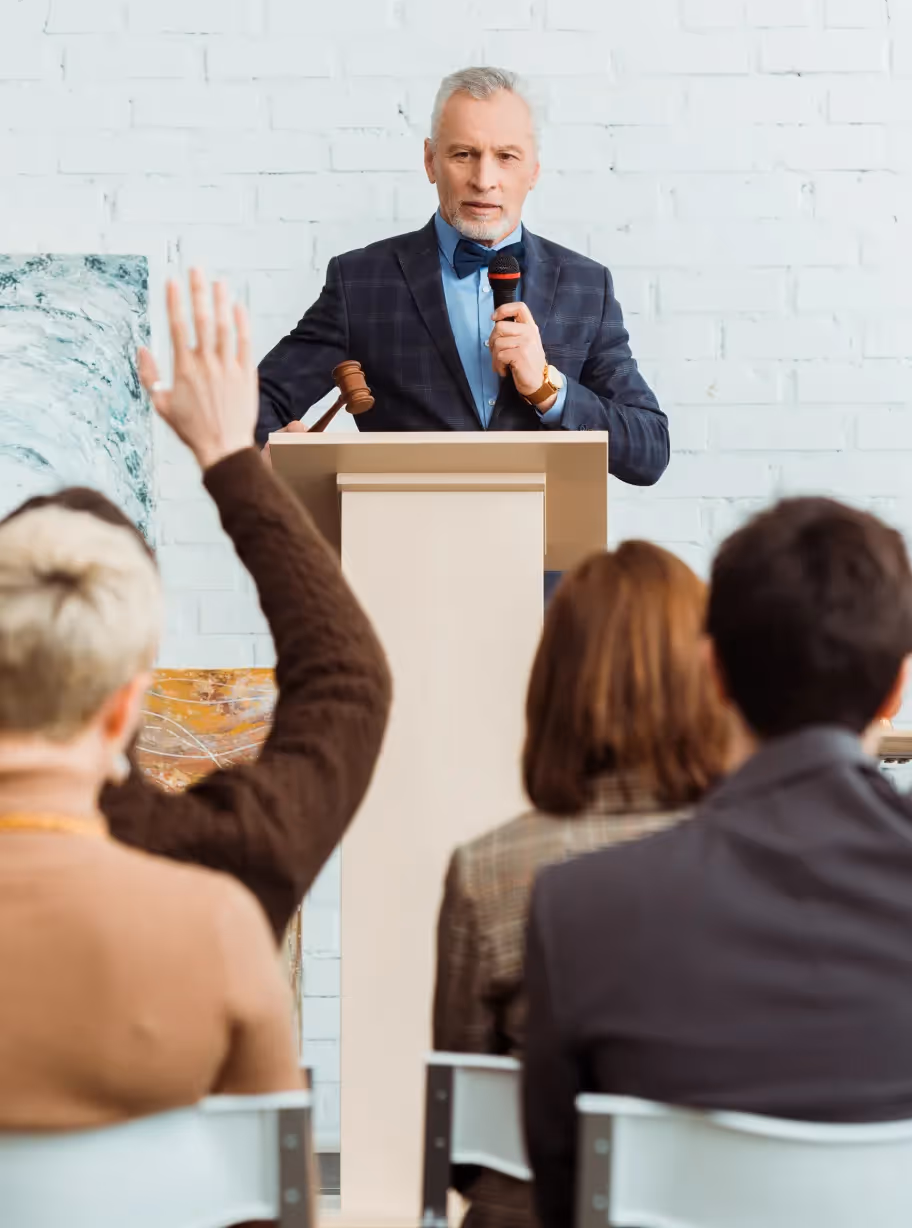 Professional auctioneer at a podium with a gavel, taking bids from an audience during a high-end art or estate auction