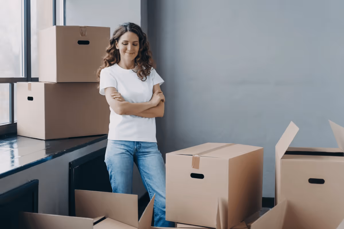 Woman standing with crossed arms in a room filled with cardboard moving boxes