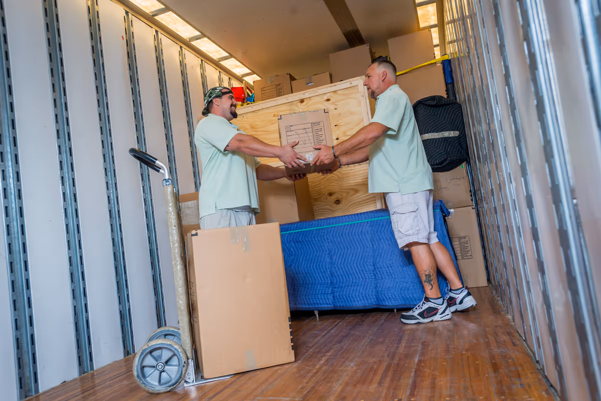 Two professional movers packing and wrapping a flat-screen television with protective materials inside a home