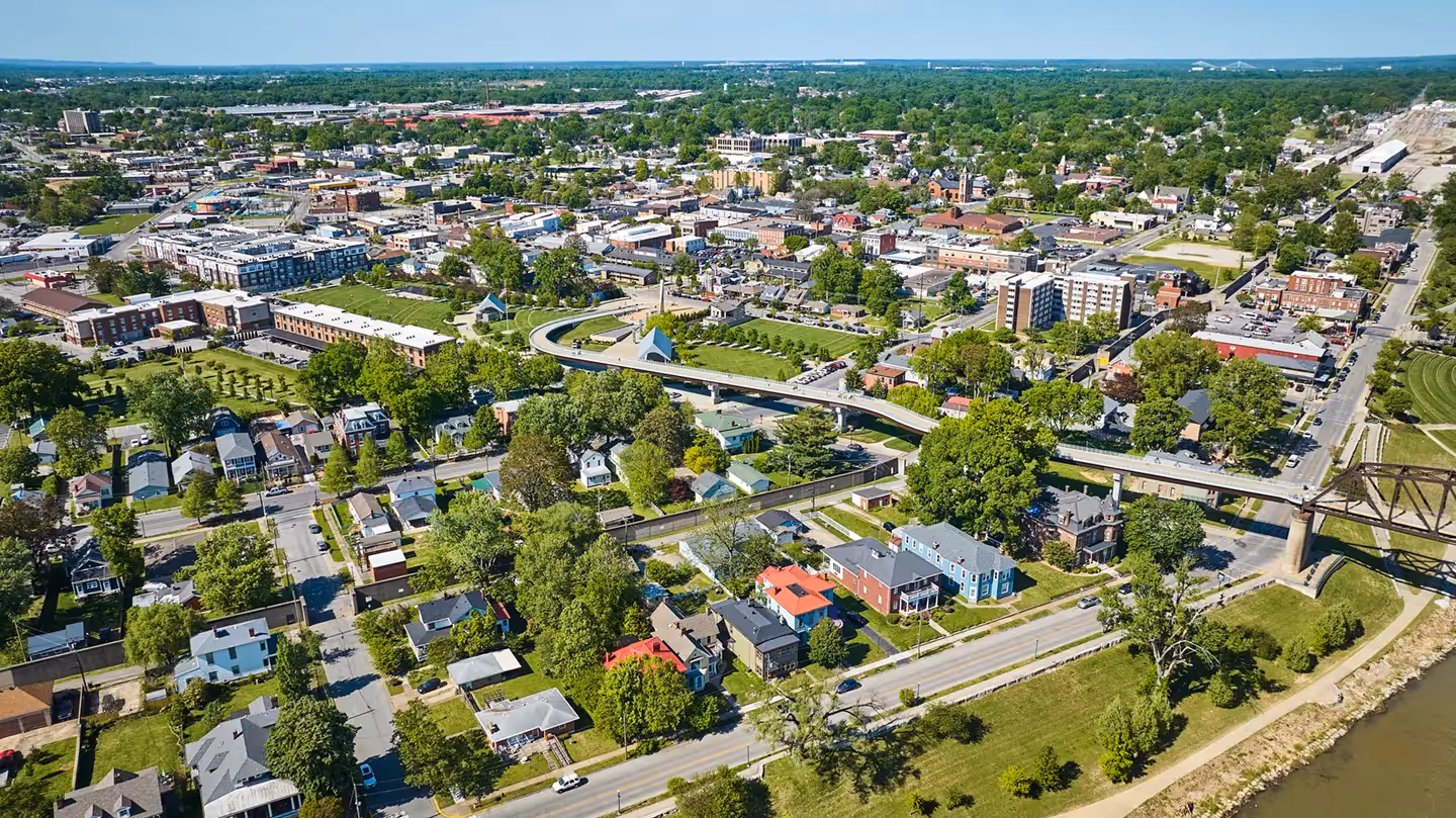 Aerial view of the downtown Louisville riverfront featuring the Big Four Bridge and surrounding green spaces