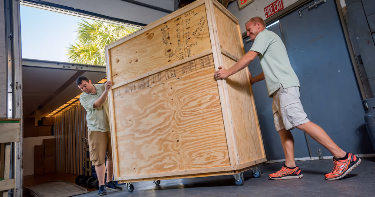 Two movers loading a large wooden shipping crate into a moving truck