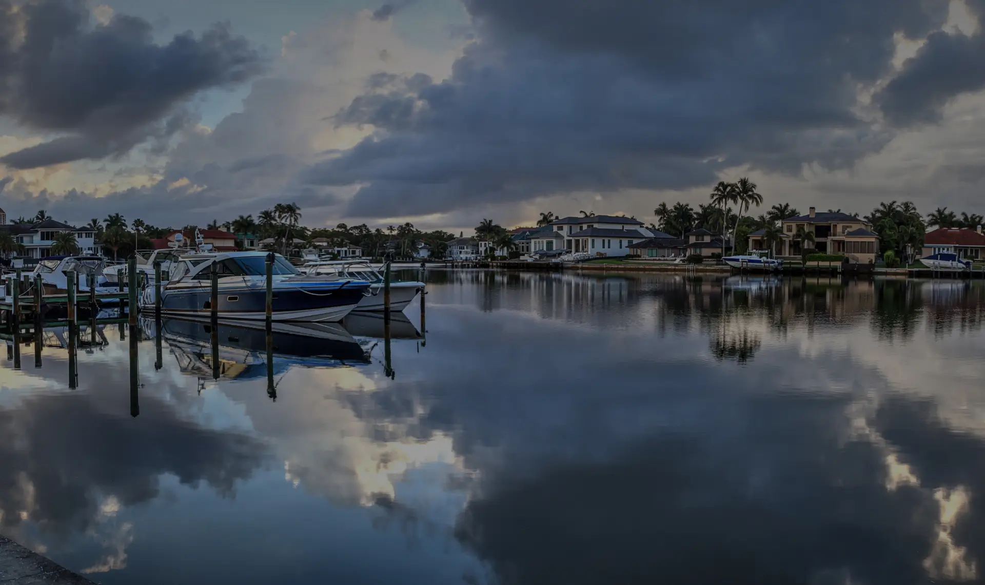 Luxury yachts docked at a North Naples marina with waterfront homes under a cloudy sky