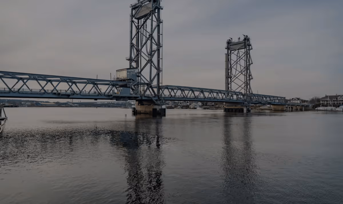 A steel vertical-lift bridge spanning a calm river under a gray sky, connecting Portsmouth and Kittery