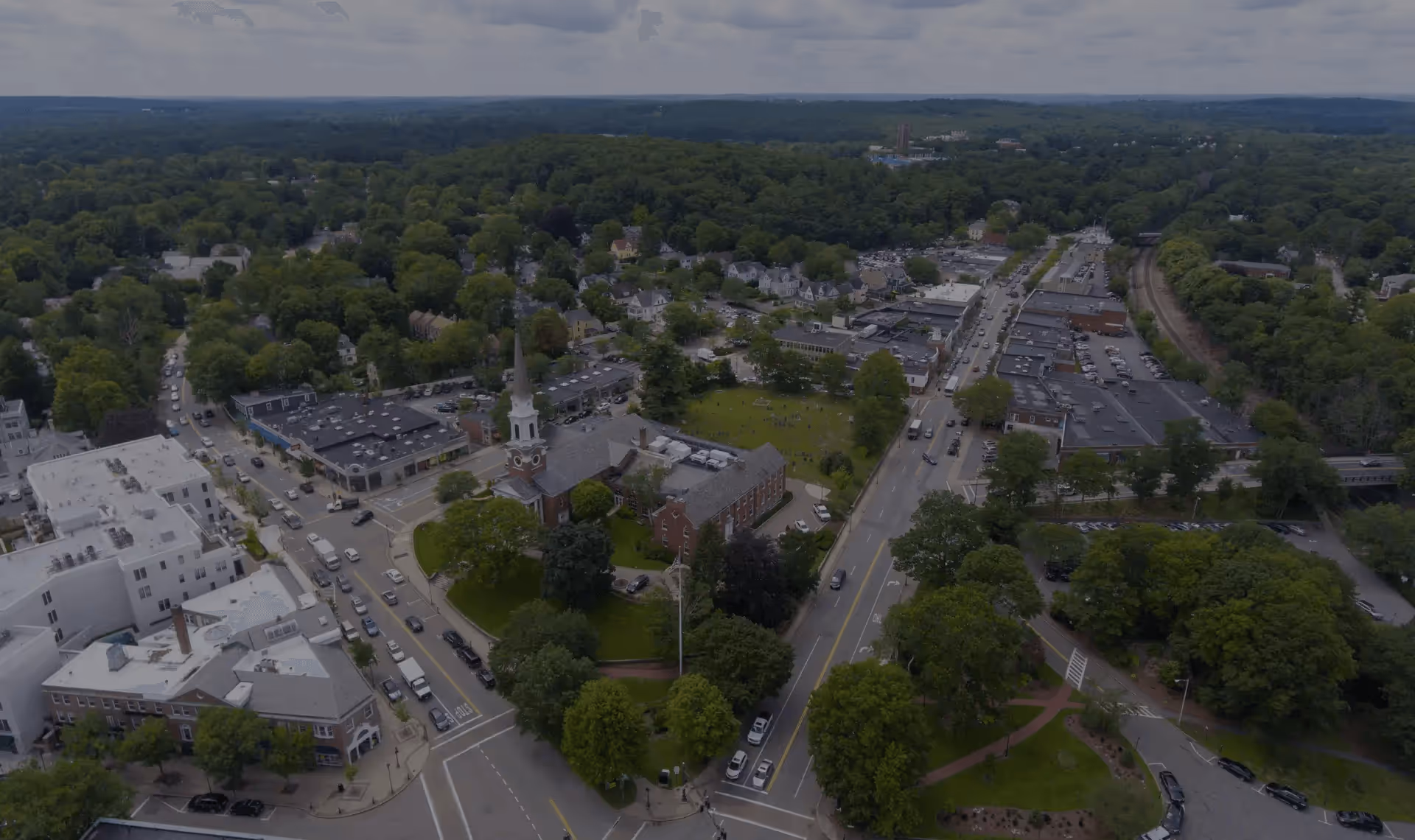 Aerial view of the Wellesley Town Hall, a historic stone building with a clock tower, surrounded by green lawns and autumn trees in Wellesley, Massachusetts