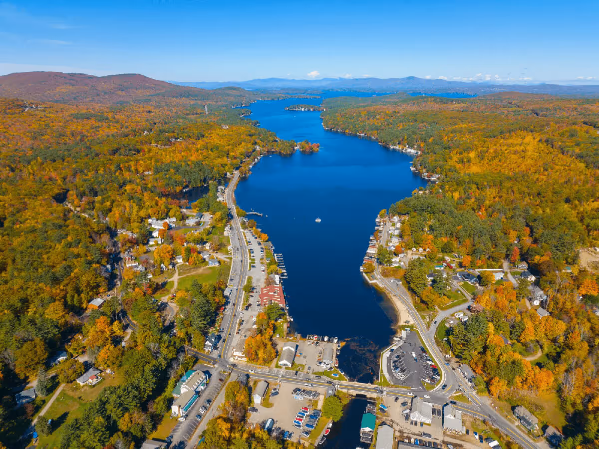 Aerial view of a coastal town featuring a marina with boats and vibrant autumn foliage along the shoreline