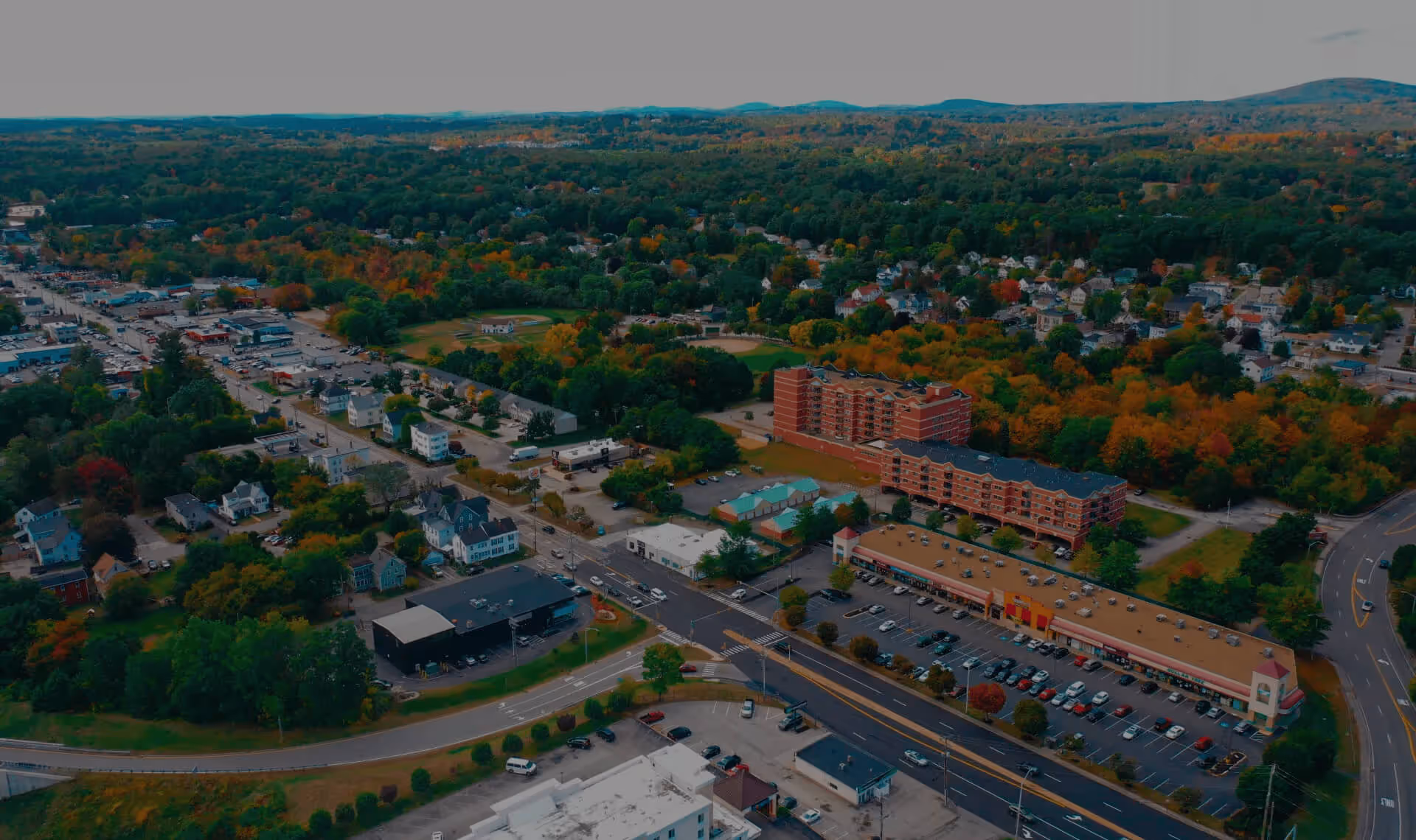 Aerial view of a suburban neighborhood with colorful autumn trees, houses, and a winding road