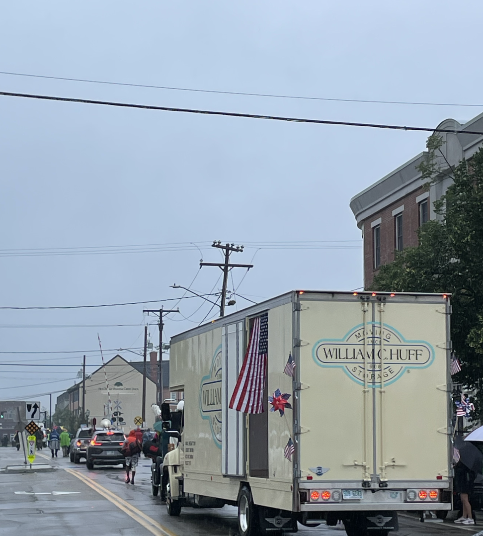 William C. Huff moving and storage truck decorated with American flags participating in a community parade on a rainy day