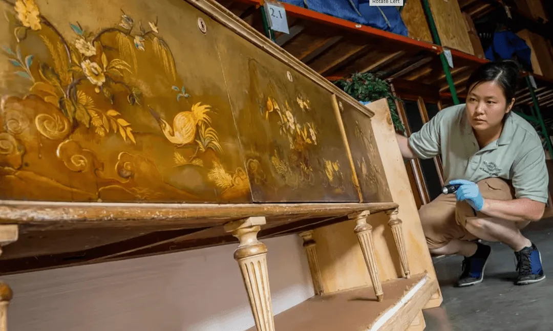 William C. Huff specialist inspecting an antique hand-painted sideboard with a flashlight