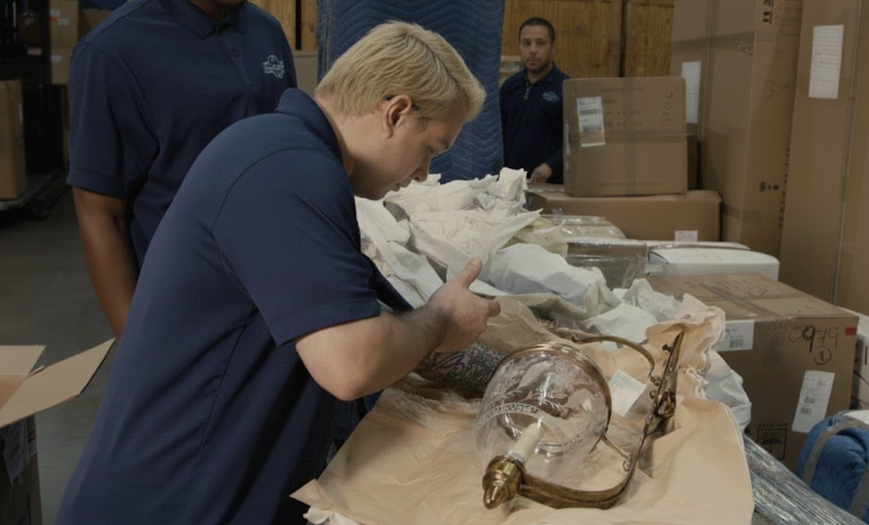 Professional movers carefully unboxing a glass light fixture in a warehouse
