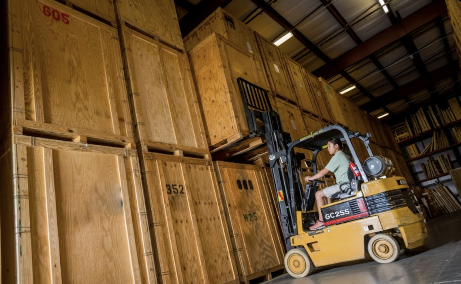 A forklift operator stacking large wooden storage crates in a high-ceiling warehouse