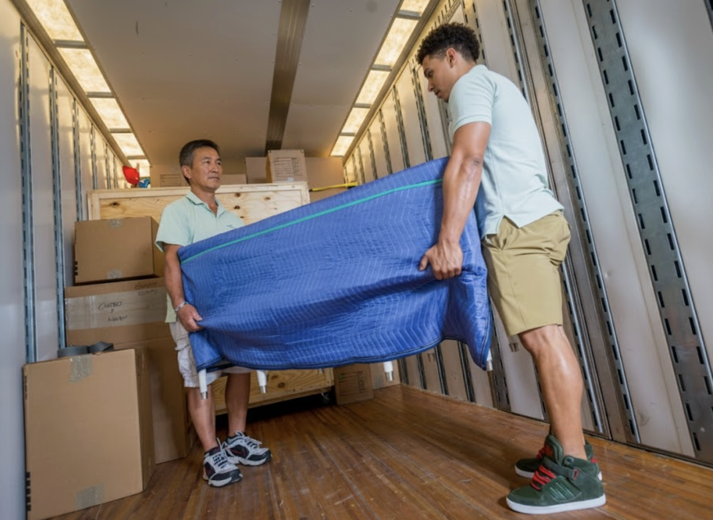 Two professional movers loading a large, blanket-wrapped piece of furniture onto a William C. Huff moving truck