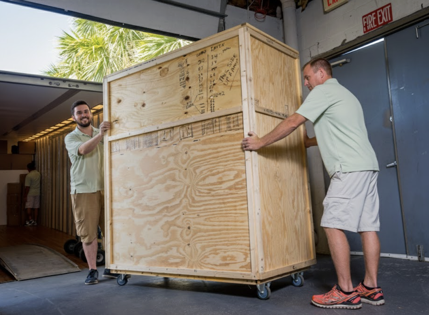 Two professional movers loading a large custom wooden storage crate onto a William C. Huff moving truck