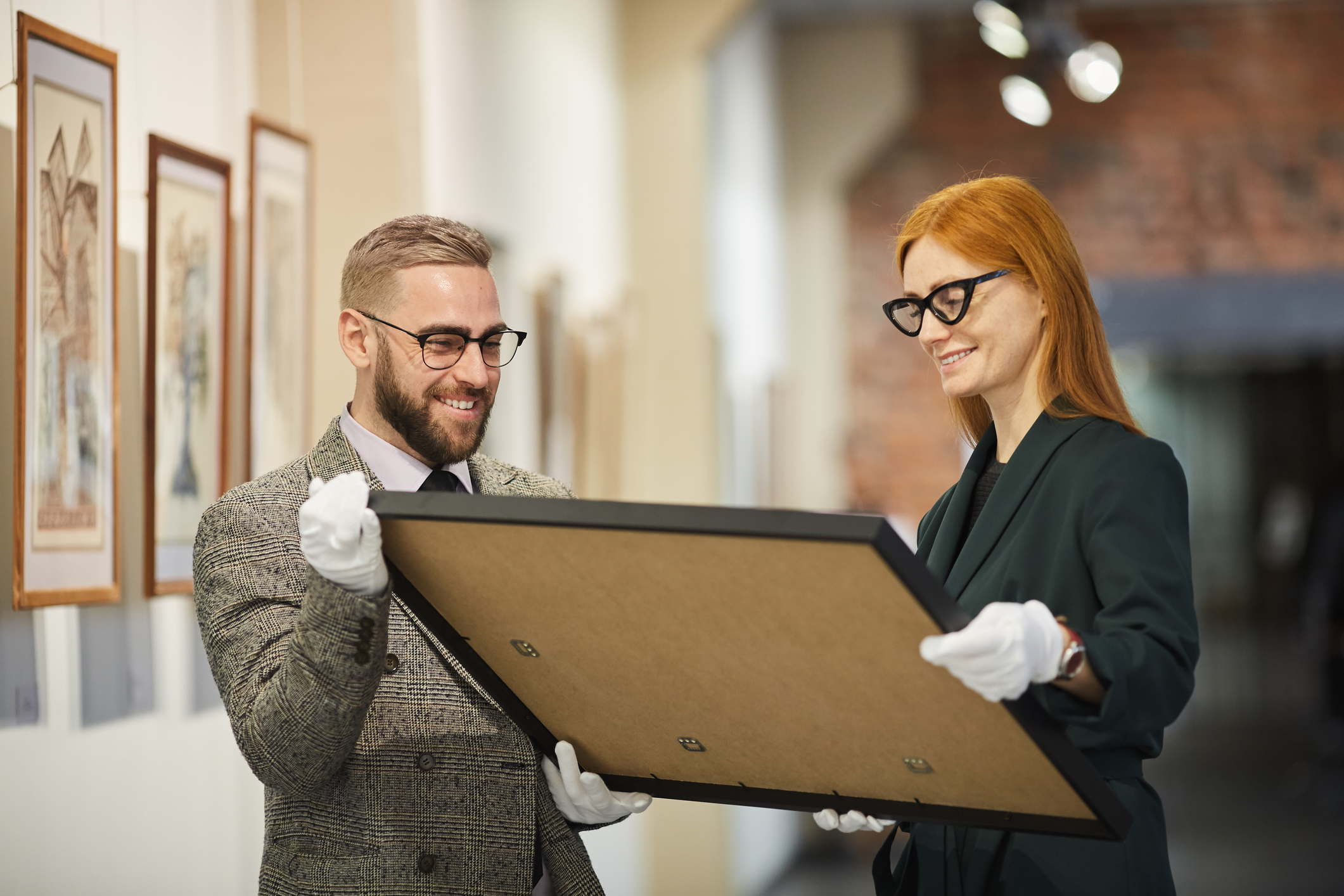 Professional art curators wearing white gloves examining the back of a framed painting in an art gallery