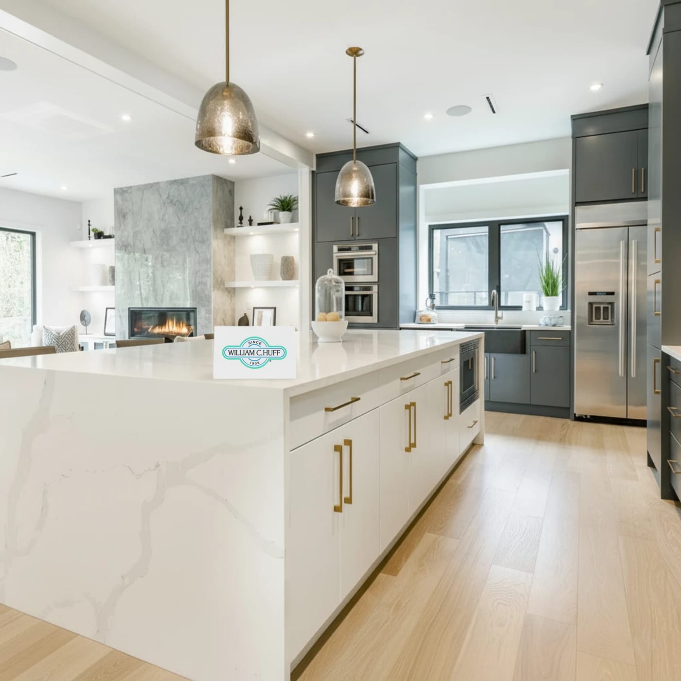 A luxury modern kitchen with a marble waterfall island and a William C. Huff sign